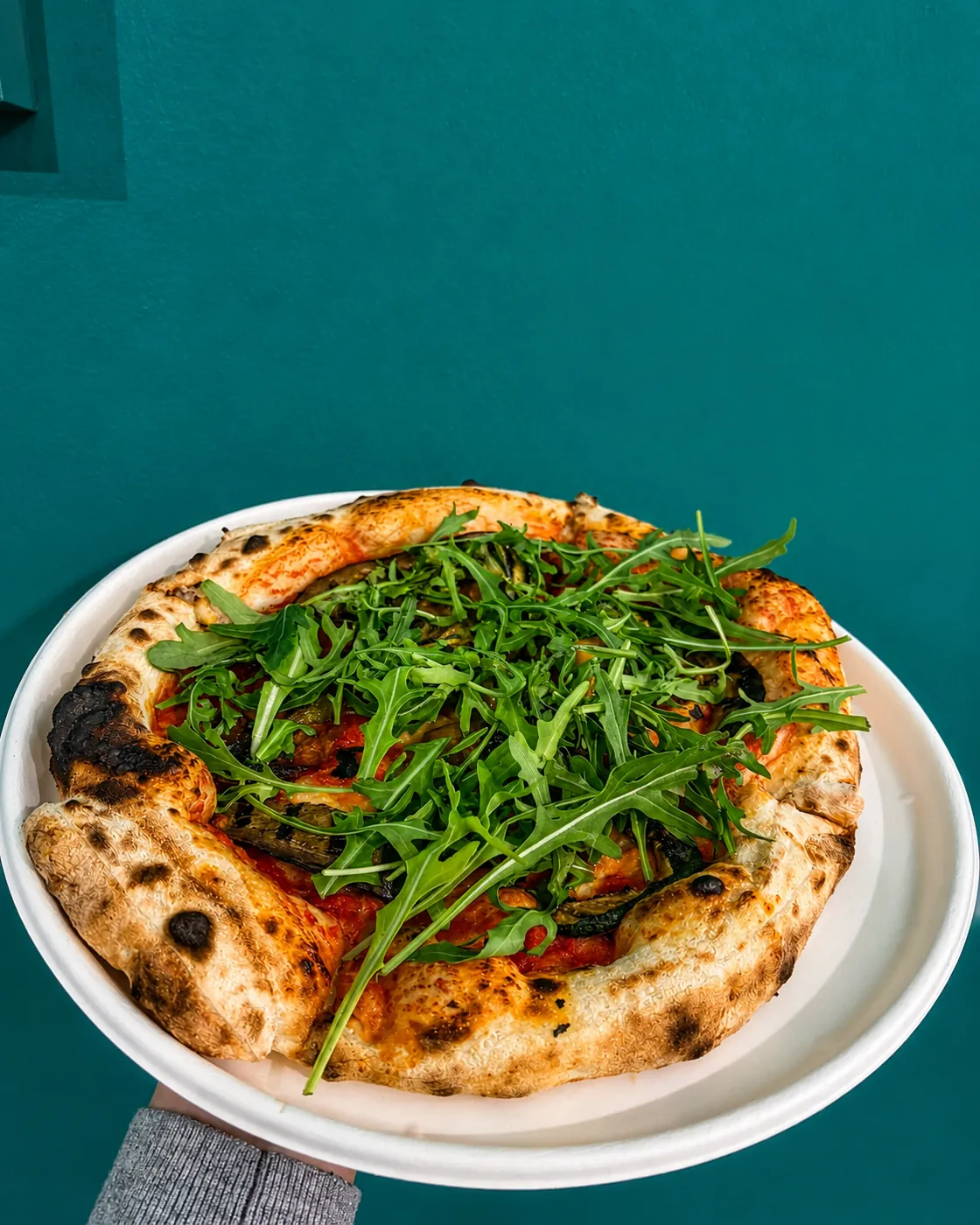 Pizza con rucola servita su sfondo verde petrolio